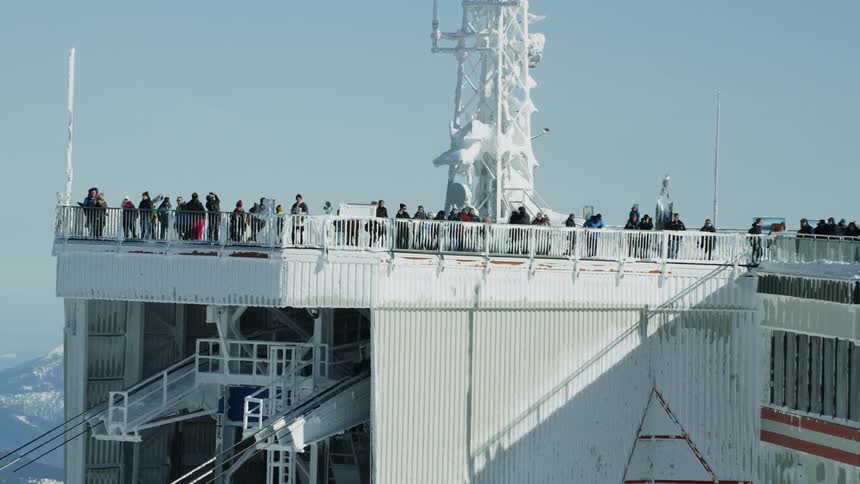 A large amount of people look out over the railing of a large mountain building