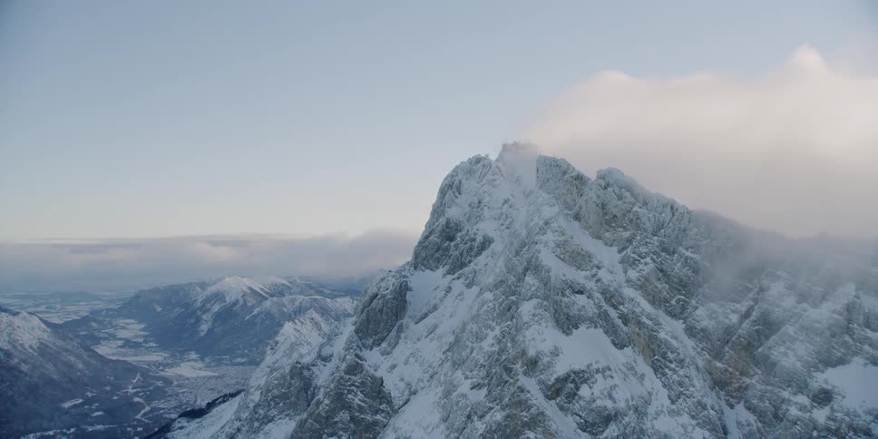 Clouds float around snowy mountains