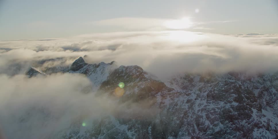 Clouds hang around and over a snowy mountain ridge