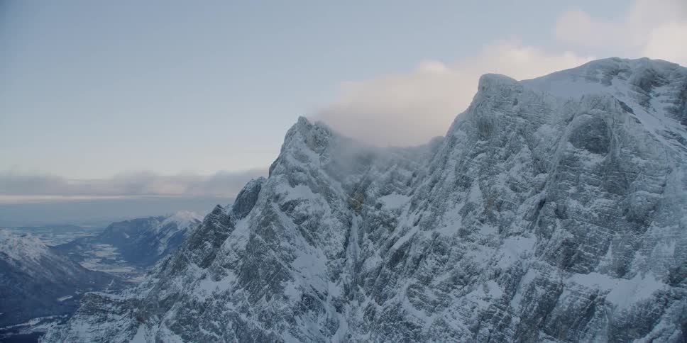 Clouds float around snowy mountains