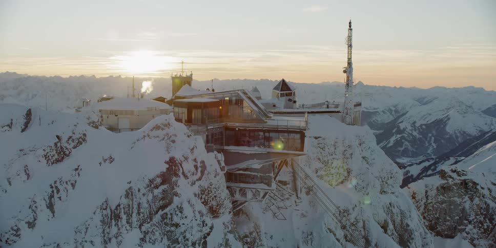 The sunlight shines on the windows of a building on a snow covered ridge
