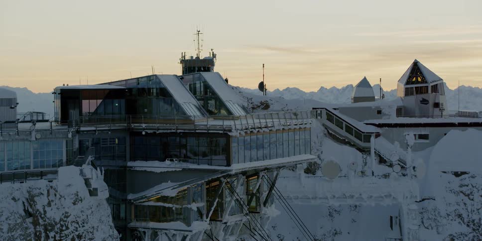 Snow covers a building in mountains at sunset