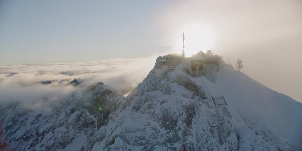 A building sits on a snowy mountain peak at sunset