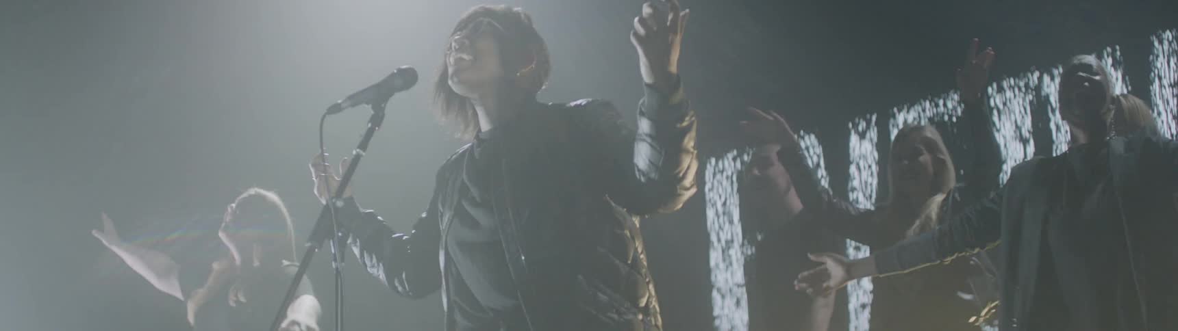 A woman sings as people dance behind her