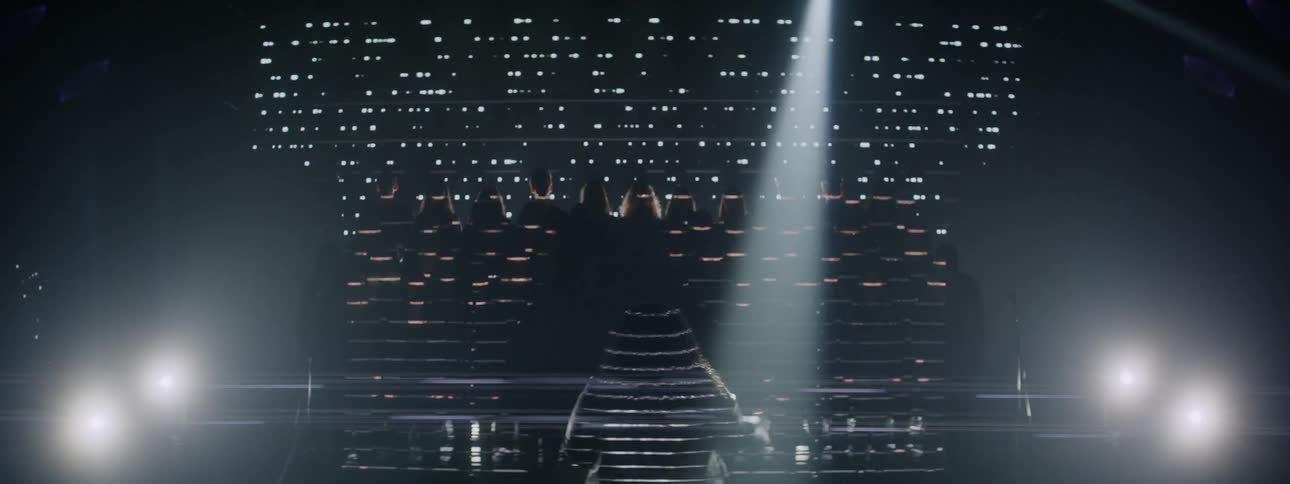 People stand on stage directed by an woman below