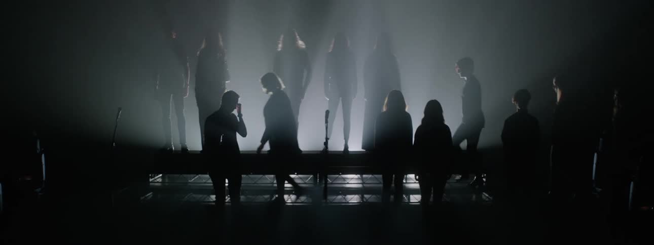 A choir files into bleachers on a dark stage