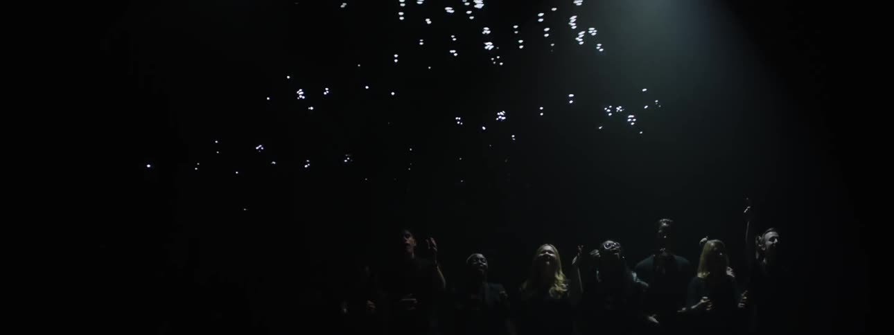 People stand in a row under flashing lights in a dark room
