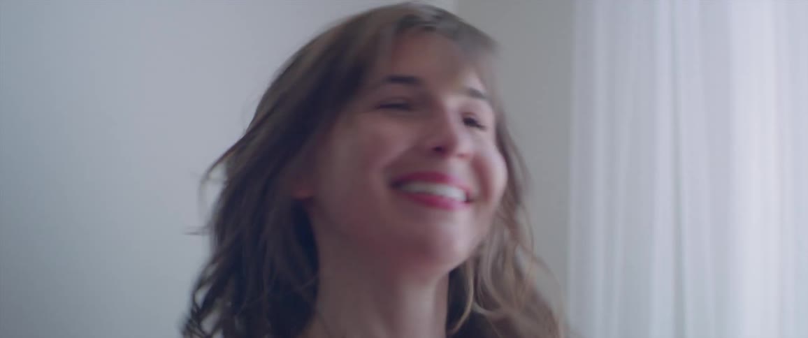 A woman smiles and dances next to a sunny window