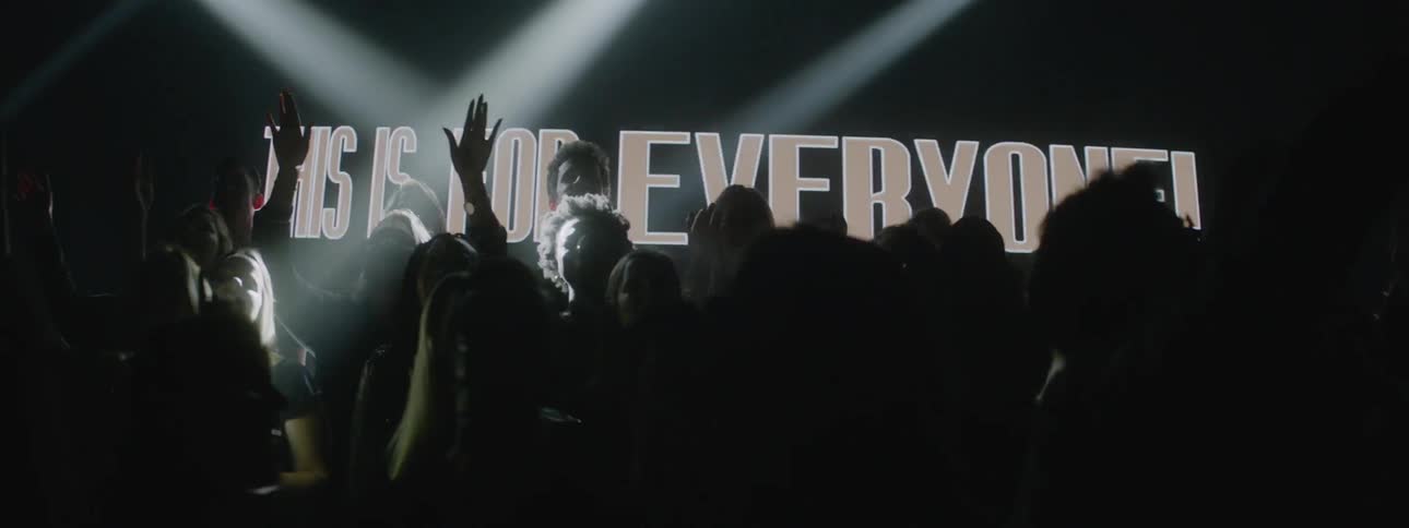 Members of a choir are raising their hands as they sing in front of projected images