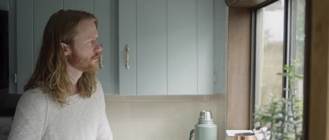 A man is staring out of his kitchen window in daylight