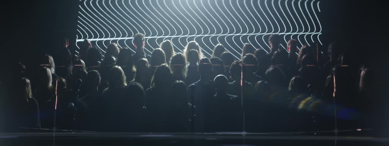A choir sings in front of flashing lights