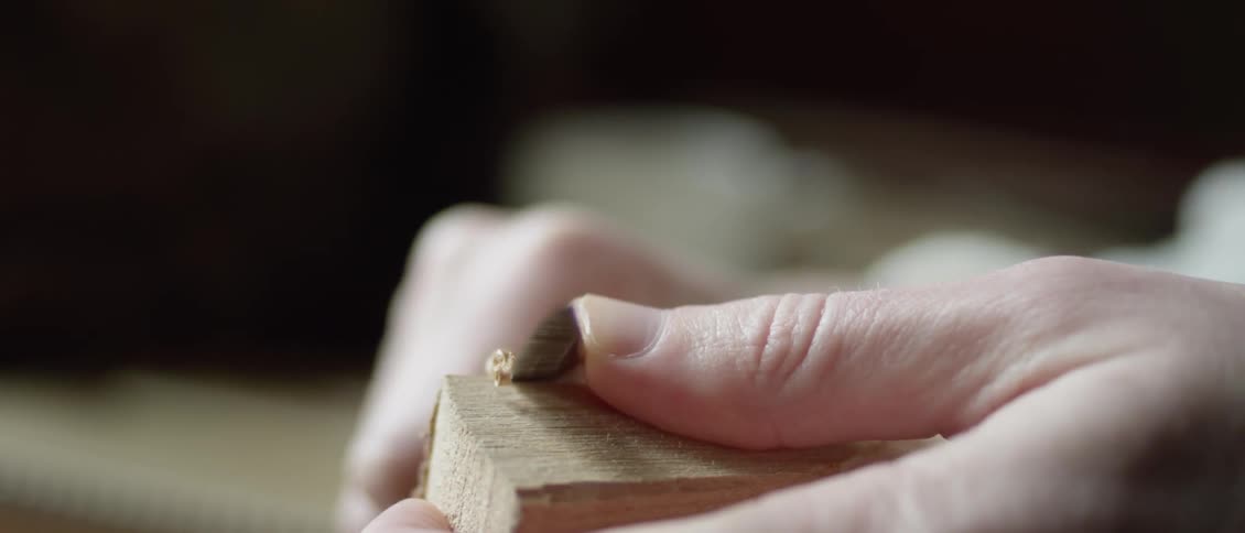 A person is whittling a piece of wood in daylight