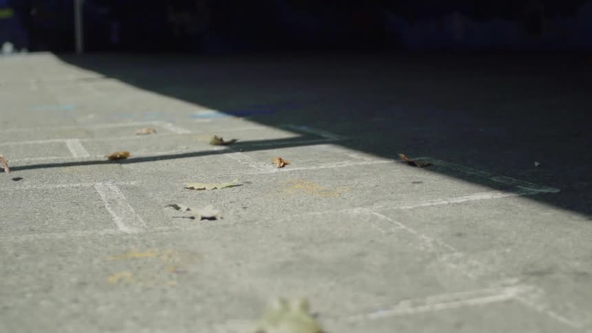 A leaf is blowing across the pavement in a schoolyard in daylight