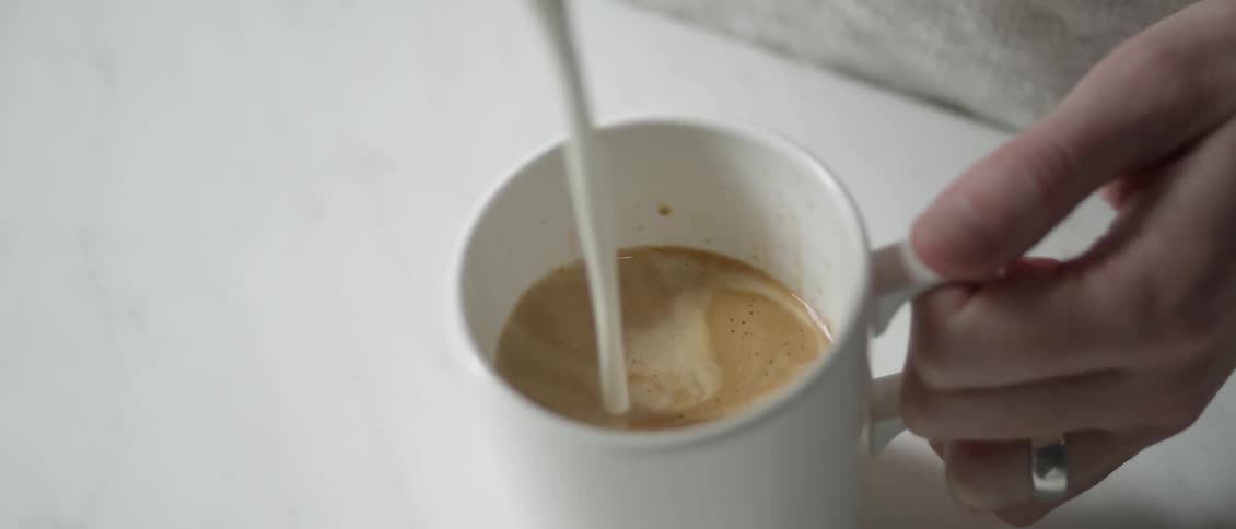A woman pours creamer into a cup of coffee