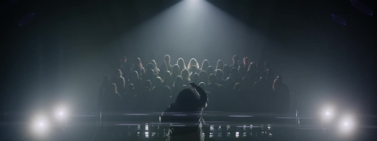 A woman conducts a choir on stage