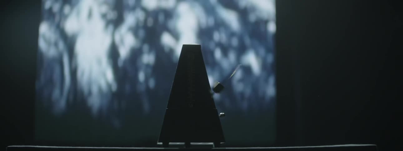 A metronome is ticking in front of a screen displaying images