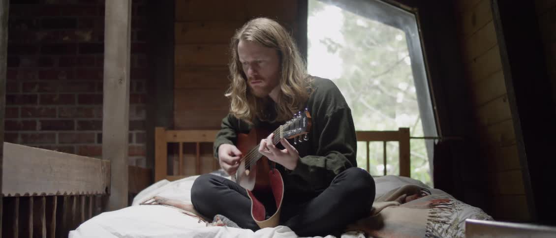 A man is sitting in bed playing guitar