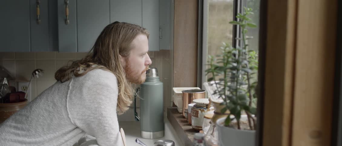 Man is leaning against kitchen counter and staring out window