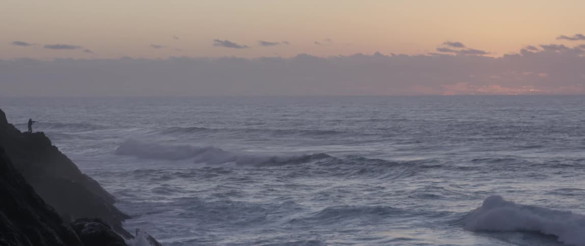Large waves rolling towards cliffs under a cloudy sky at sunset
