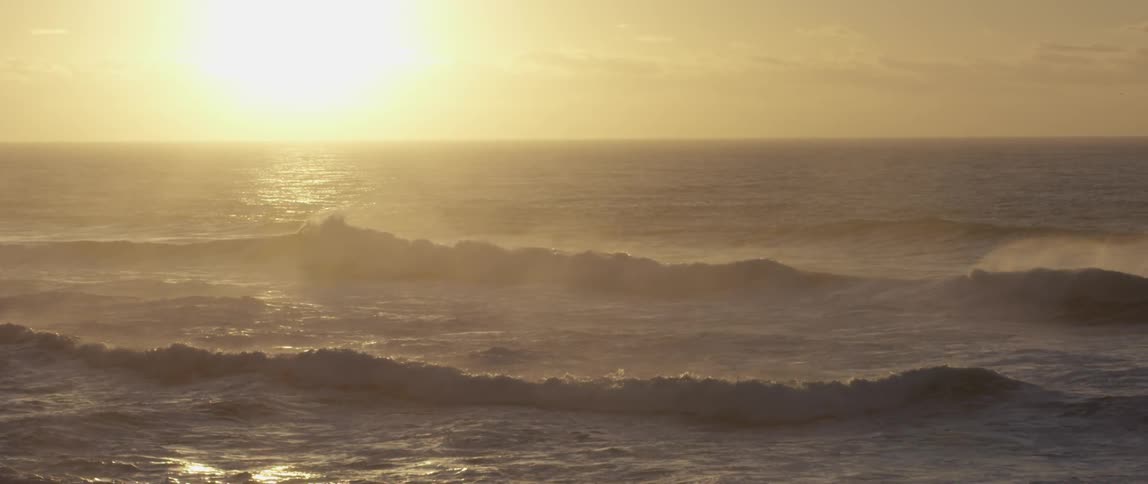 Ocean waves break against the shore as the sun goes down over the sea