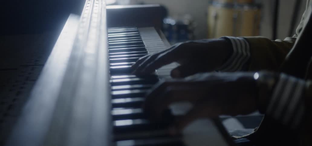 A man is playing an upright piano inside in daylight