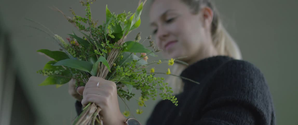 A young, blonde woman holding a bunch of flowers and turning her head to smile