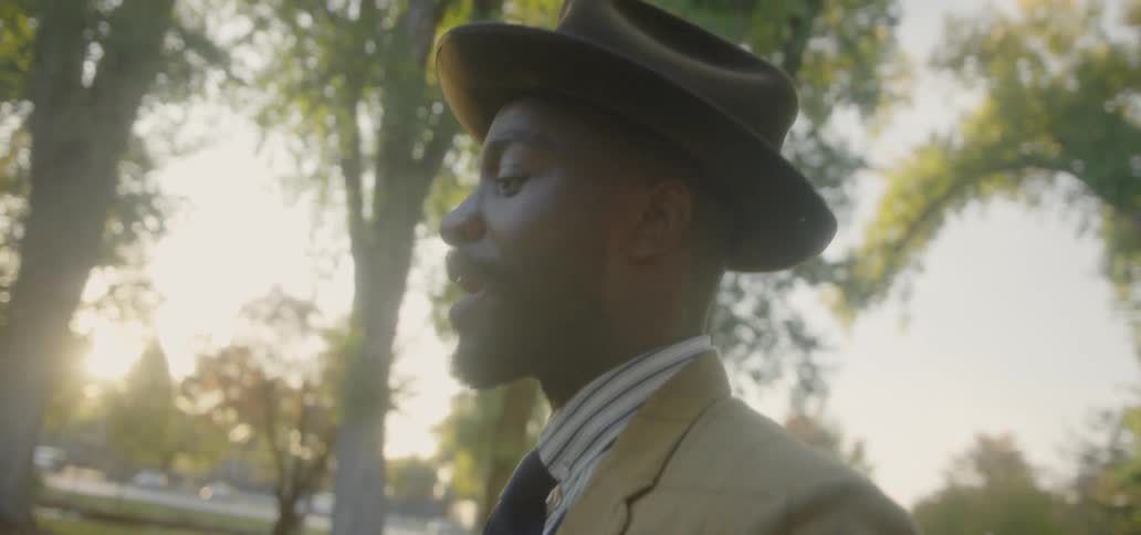 A man in a suit and tie walks outside under the trees