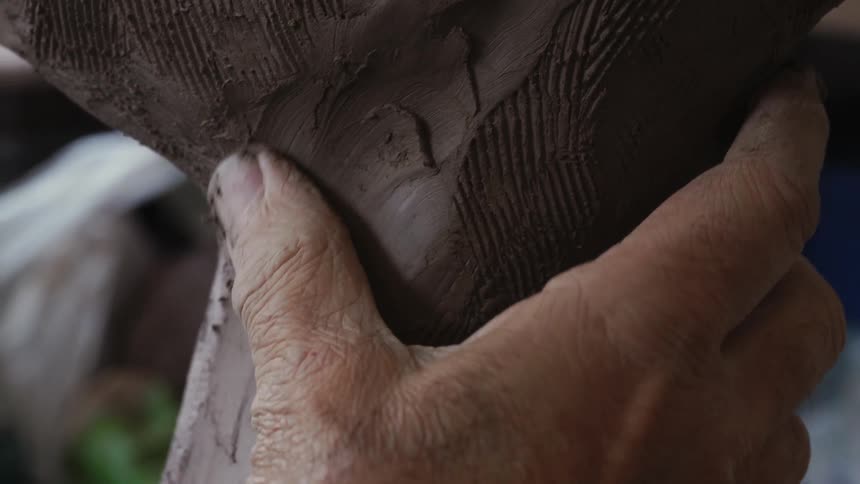 A sculptor models clay with their hand
