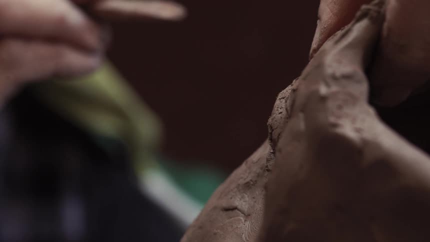 A person is using a wooden chisel to sculpt clay