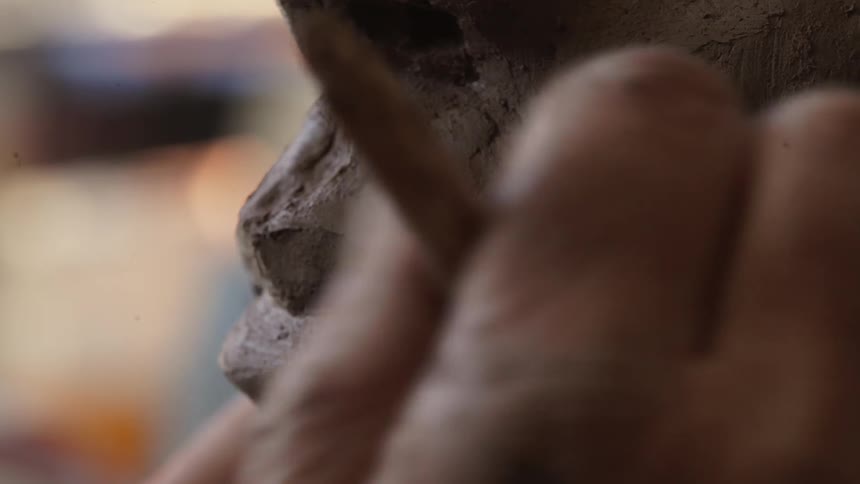 A sculptor models clay with their hand