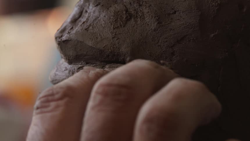 A sculptor models clay with their hand