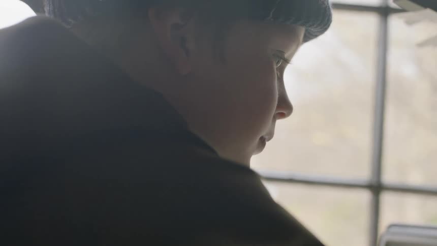 A boy is sitting at the table by the window