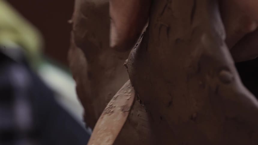 A sculptor models clay with a tool