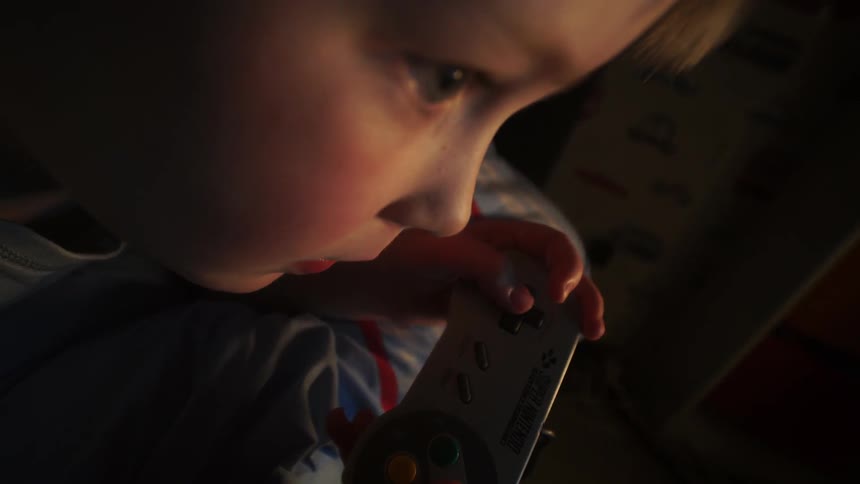 A young boy lays on a bed at night playing a video game in the dark