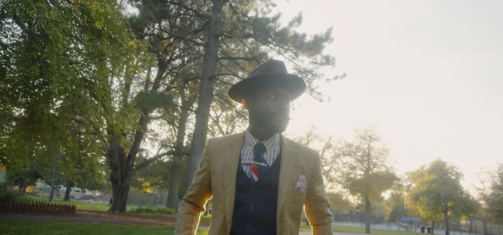 Man wears a hat and suit outside at sunset