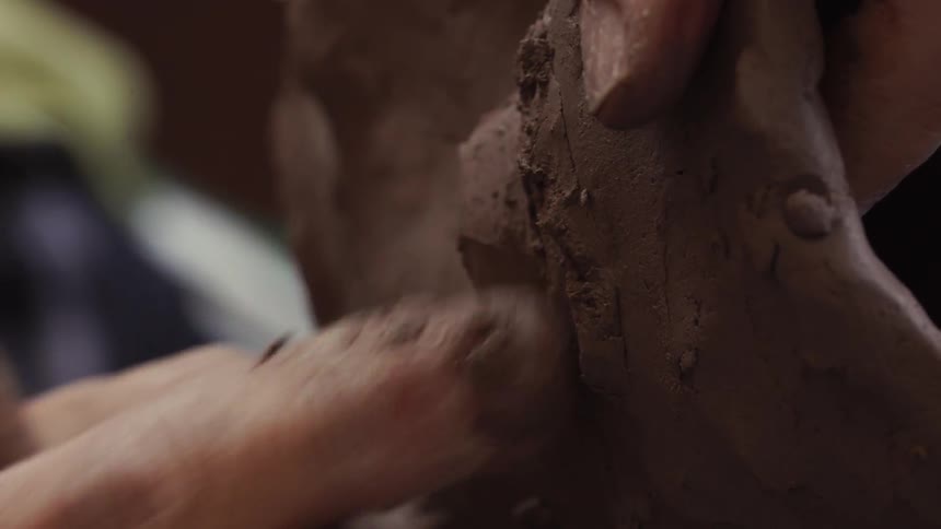 A sculptor models clay with their fingers
