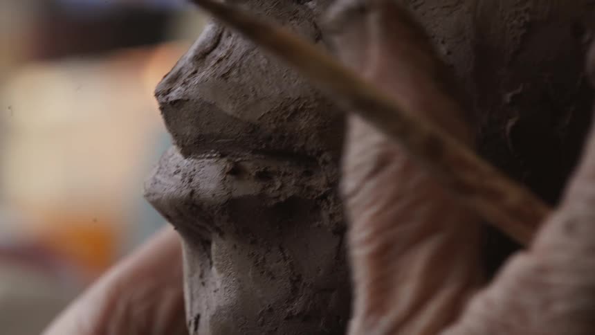 A sculptor models clay with their finger