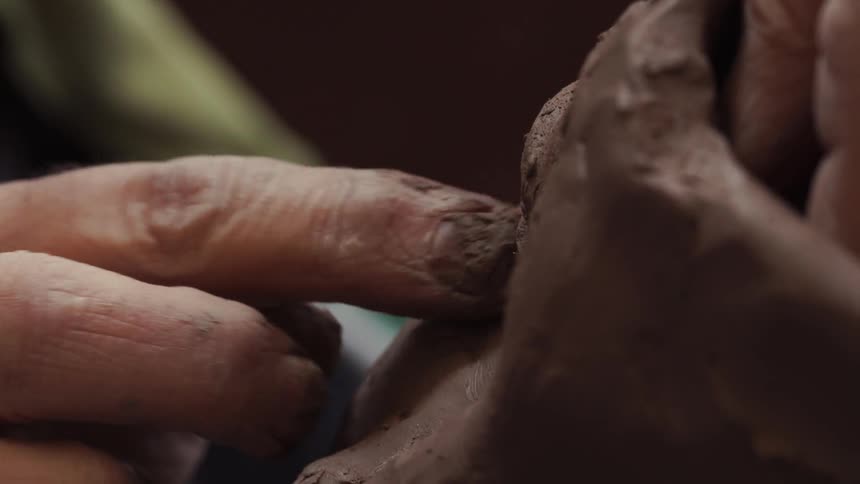 A sculptor is forming some clay with finger pats