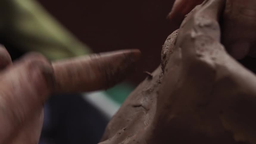 Person using wooden tool to sculpt an eye on clay face