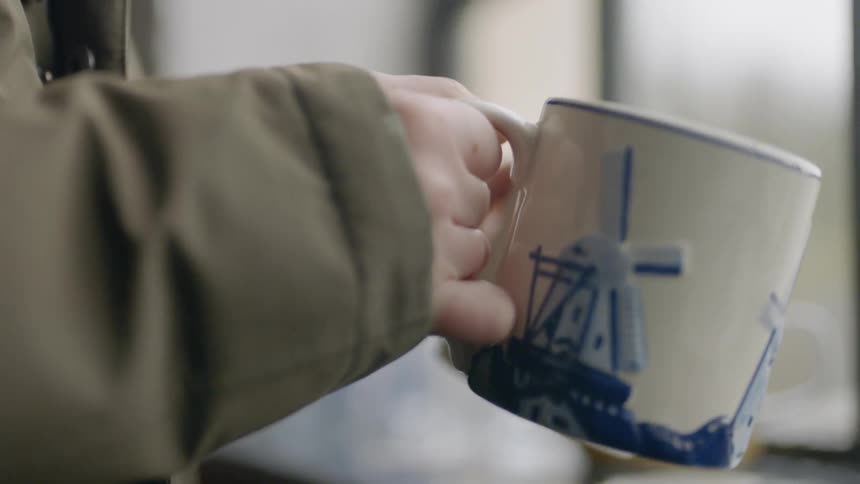 A person holds a mug next to a window