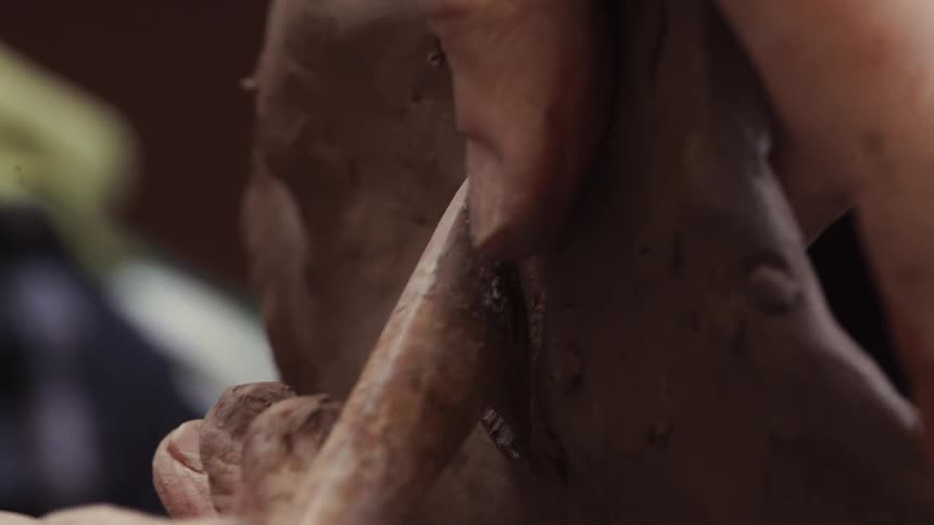 A sculptor models clay with a tool