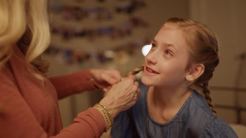 A girl smiles as her mom braids her hair