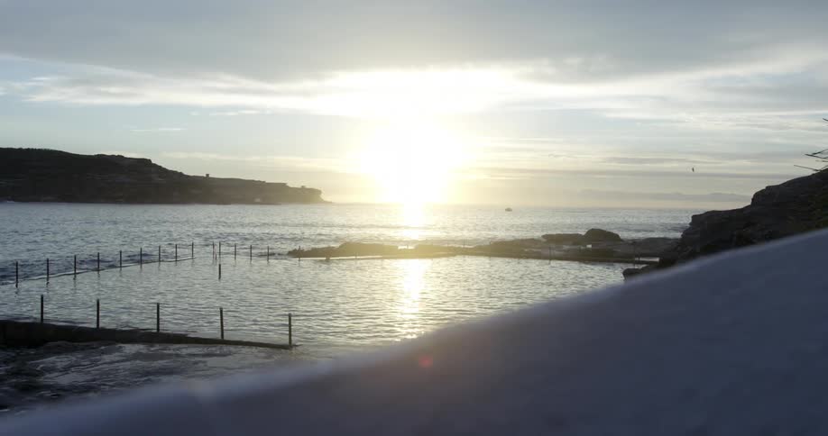 View from above as a person swims by the shore and the sun rises