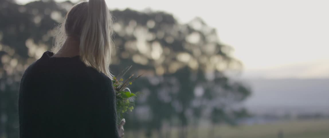 A blonde woman standing outdoors holding a bunch of flowers