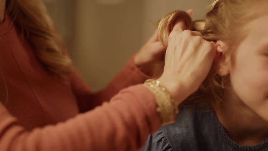 A mother is braiding her daughter's hair inside a bedroom