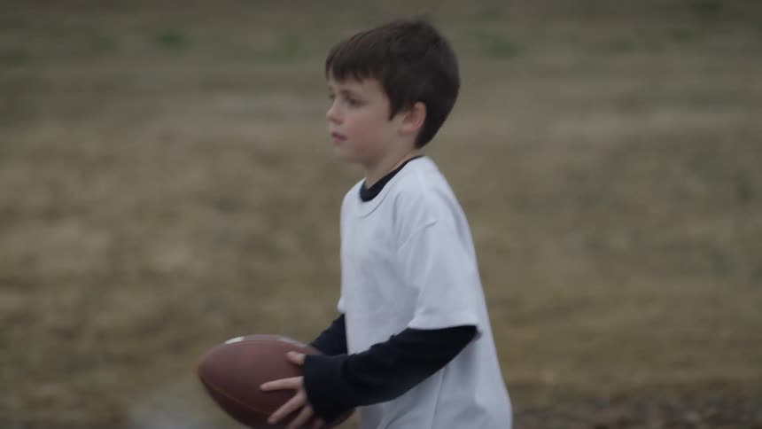 The boy walks along the field holding a football