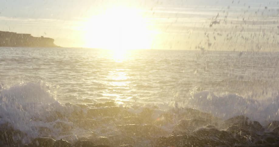 Waves crash onto a rocky beach at sunset