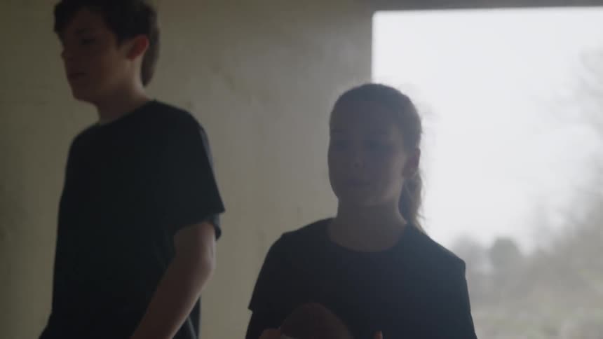 Teen boy and girl walking into a tunnel as the girl tosses a football in the air to herself