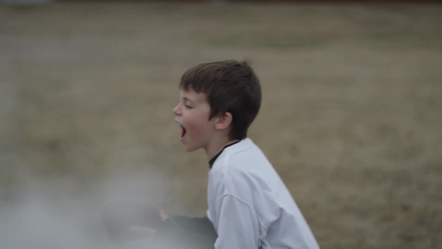 Little boy is yelling out while running and holding football on foggy day