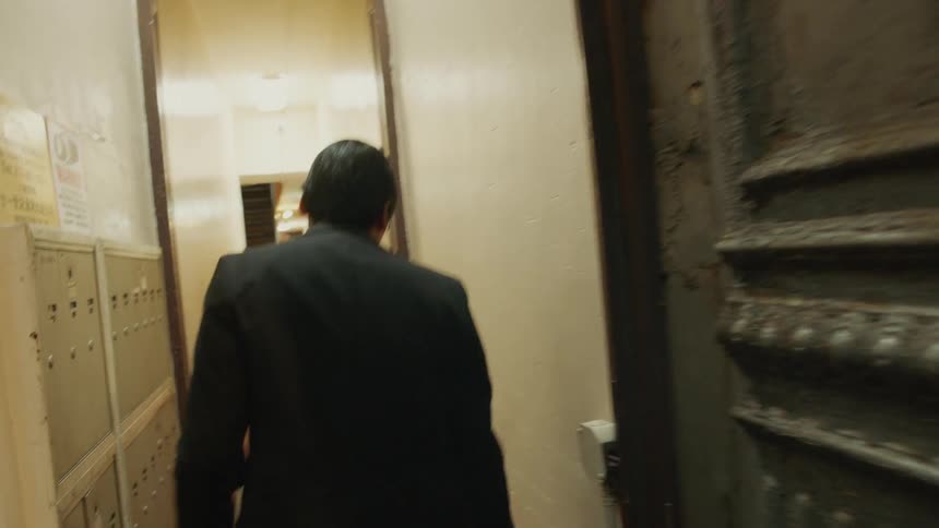 Man enters an apartment building and walks down hallway